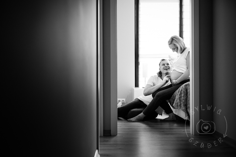 kobieta w ciązy siedzi na łóżku w sypialni z mężem u jej stóp - sesja ciążowa Warszawa