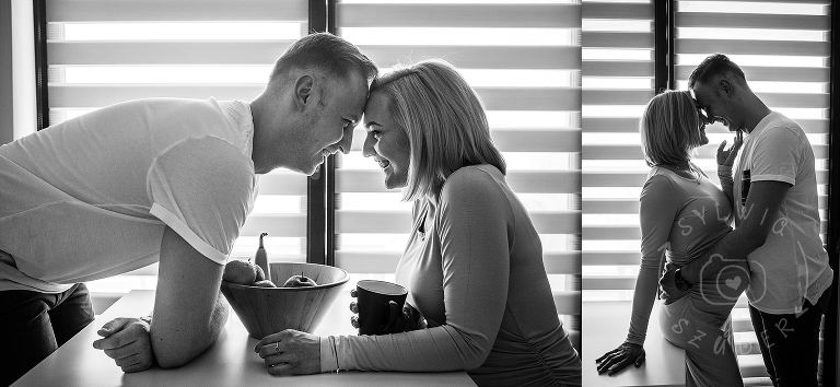 kobieta w ciązy i jej partner całują sie w swojej kuchni na tle okna z żaluzjami