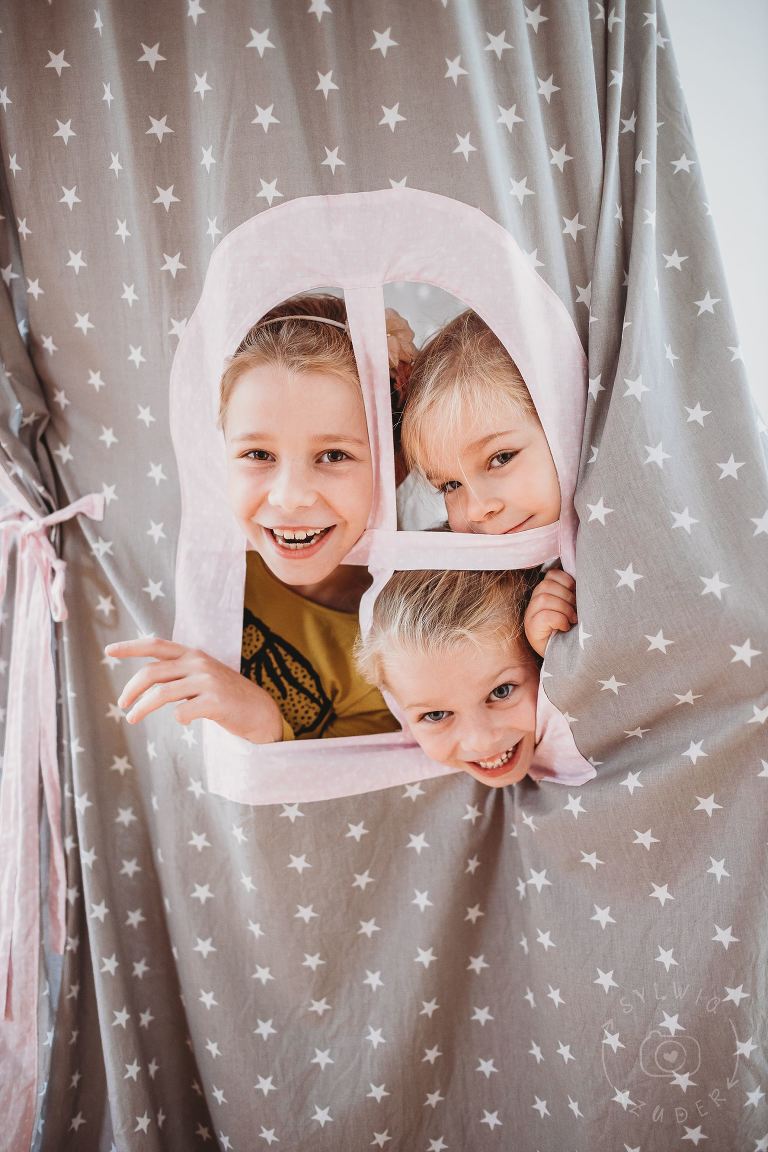 trzy dziewczynki wyglądają przez okno namiotu