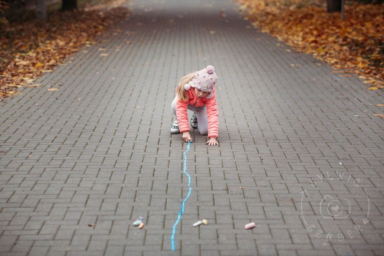 dziewczynka rysuje długą, prostą kreskę kredą po chodniku
