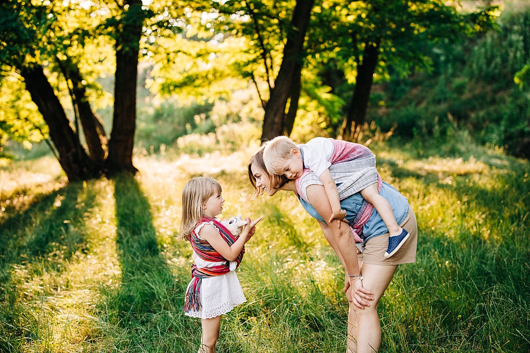 mama z synkiem na plecach w chuście rozmawia z córeczką, która zamotała w chustę swoją przytulankę